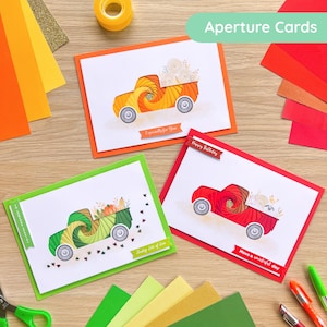 May include: Three greeting cards with truck illustrations in orange, green, and red. Each card has a different message: "Especially for You", "Sending lots of love", and "Have a wonderful day". The cards are on a wooden surface.