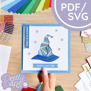 May include: A blue and gray papercraft wizard hat with a white background and the text "Happy Birthday" and "Have a magical day!"  The hat is surrounded by silver glitter stars.