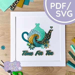 May include: A teal and gold paper craft of a teapot with the words "Time For Tea" in gold glitter letters. The teapot is surrounded by teal and gold paper flowers.