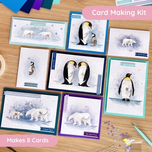 May include: A card making kit with eight cards featuring polar bears and penguins. The cards have blue, teal, and purple borders. The text "Card Making Kit" is in a pink oval. The text "Makes 8 Cards" is in a pink oval.