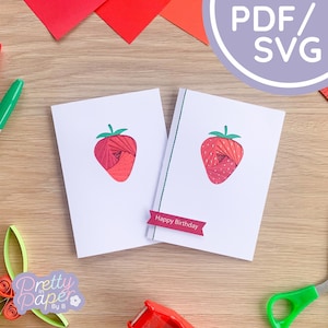 May include: Two white greeting cards with a red paper strawberry design and green stem. One card has a banner that reads "Happy Birthday". The cards are on a wooden surface with craft supplies.