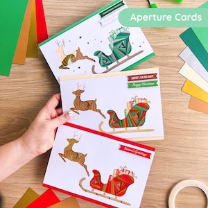 Puede incluir: Tarjetas de felicitación navideñas con un reno tirando de un trineo lleno de regalos. Las tarjetas tienen el texto "Christmas Wishes", "Santa's on his way! Happy Christmas" y "Season's Greetings". Tarjetas blancas con detalles rojos, verdes y dorados.