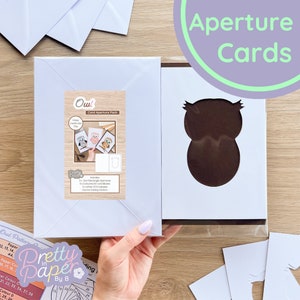 Puede incluir: Un conjunto de tarjetas de apertura de búho para manualidades. El conjunto incluye tres tarjetas blancas en blanco, tres recortes de apertura de búho y un sobre blanco. Las tarjetas en blanco se muestran con búhos de diferentes colores. El texto en el paquete dice "Owl Card Aperture Pack" e "Incluye: 3x Aperturas rectangulares de búho, 3x Blancos de tarjetas A4, 1x Sobre blanco C5, Patrón de plegado de iris de búho".