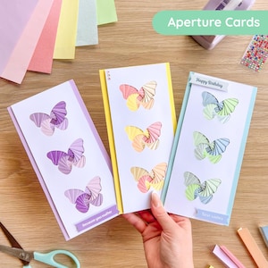 May include: Three handmade aperture cards with butterfly cutouts. The cards feature a white background with colorful butterfly designs in shades of purple, yellow, and pastel colors. The text "Aperture Cards" is visible at the top. One card has the text "Because you matter" and another says "Happy Birthday".