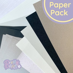 May include: A pack of paper featuring different colours and textures, including white, grey, black, and brown. The paper is arranged in a fan shape, with the text "Paper Pack" in a purple circle at the top of the image. The text "Pretty in Paper By B" is in the bottom left corner of the image.
