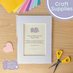 Puede incluir: Un juego de 3 marcos de fotos blancos con el texto "Picture Mount Set of 3 Bright White". El borde exterior mide 210 mm de ancho y 297 mm de alto. También se ven unas tijeras amarillas y papel de manualidades de colores.