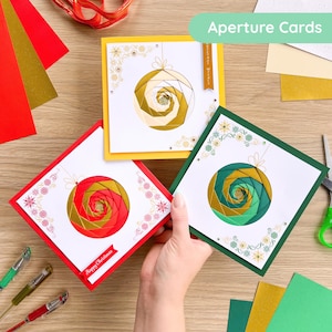 May include: Three handmade Christmas cards with geometric bauble designs. The cards have red, yellow, and green borders. Each card features a different colour scheme for the bauble, with gold accents and decorative floral patterns.