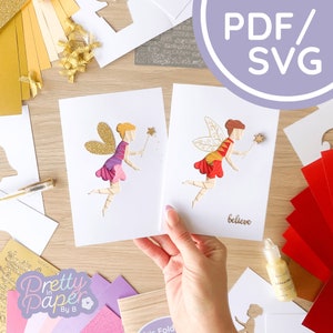May include: Two papercraft fairy cards with intricate details. The card on the left features a fairy with purple and pink wings and a gold glitter wand. The card on the right features a fairy with red and yellow wings and a gold glitter wand. The card on the right also has the word "believe" written on it.