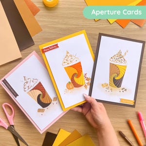 Puede incluir: Tres tarjetas de felicitación con un diseño temático de café. Cada tarjeta presenta un diseño en espiral en tonos marrones, naranjas y amarillos, cubierto con crema batida. Una tarjeta dice "Happy Birthday", otra "Best Wishes".