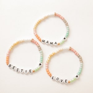May include: Three colourful beaded bracelets with the words "BESTIE", "MAMA", and "LOVE" spelled out in white beads. Each bracelet has a small heart charm.