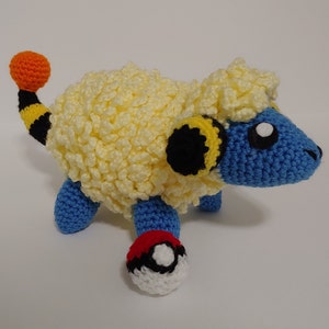 May include: A blue and yellow crocheted Pokemon plush toy with a fluffy white mane. The toy is holding a red and white Pokeball.