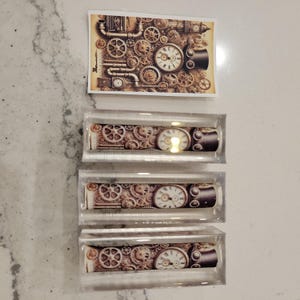 May include: Three clear acrylic tubes with a steampunk design image inside. The image features a clock face, gears, and pipes.