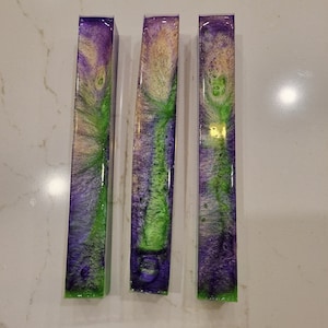 May include: Three long, rectangular resin blanks with a swirling pattern of purple, green, and white.