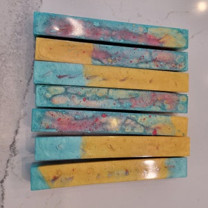 Puede incluir: Siete barras rectangulares con un diseño abstracto colorido. Las barras alternan entre turquesa y dorado. Las secciones turquesas tienen un efecto acuarela moteado con acentos rosas y amarillos.