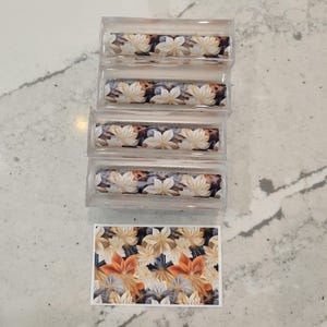 May include: Four clear plastic tubes with a floral pattern printed on them. The pattern features beige, orange, and blue flowers. A separate sheet of paper with the same floral pattern is also shown.