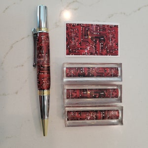 May include: A silver pen with a red and gold circuit board design. The pen is displayed with three small rectangular boxes, each with a similar circuit board design.