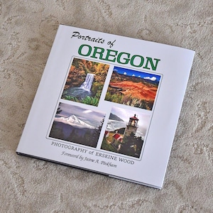 May include: A square book titled "Portraits of Oregon" with four landscape photographs. The cover features a waterfall, desert landscape, mountain, and a lighthouse. The text "Photography of Erskine Wood" and "Foreword by Jaime A. Pinkham" are also visible.
