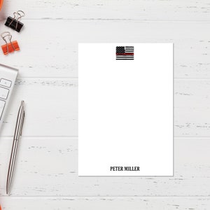 May include: White notepad with a black and white American flag with a red stripe across the middle. The text "PETER MILLER" is printed at the bottom of the notepad.