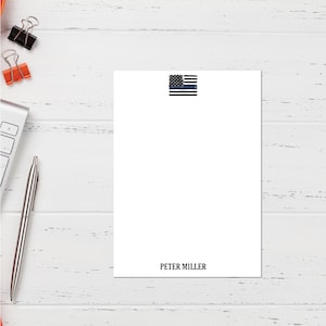 May include: A white notepad with a thin blue line American flag in the top right corner and the name "PETER MILLER" printed at the bottom.