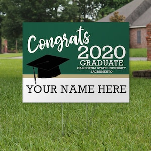 May include: Green and white yard sign with the text "Congrats 2020 Graduate California State University Sacramento" and "Your Name Here". A black graduation cap is on the sign.