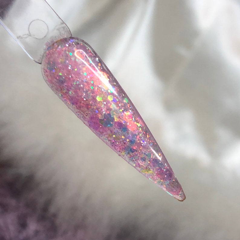 May include: A close-up of a pink nail polish with iridescent glitter. The polish is applied to a long, pointed nail.