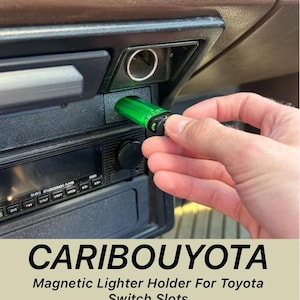 May include: A green magnetic lighter holder is inserted into a Toyota switch slot. The holder is cylindrical with a black top. The text "CARIBOUYOTA" and "Magnetic Lighter Holder For Toyota Switch Slots" are displayed below the car's dashboard.