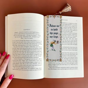 May include: A close-up of a book with a bookmark. The bookmark is a colorful illustration of a person holding a scroll. The text on the bookmark reads "Allow me to hold thy page, my liege."