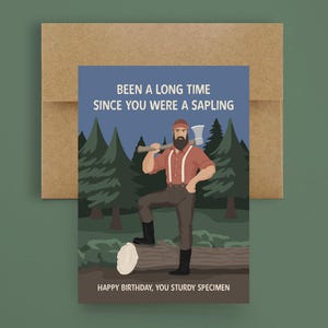 May include: Greeting card with a cartoon illustration of a lumberjack holding an axe, with the text "BEEN A LONG TIME SINCE YOU WERE A SAPLING" and "HAPPY BIRTHDAY, YOU STURDY SPECIMEN". The card is paired with a brown envelope.
