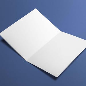 May include: A blank, open greeting card with a white interior, resting on a blue surface. The card is slightly angled, showcasing its unfolded design. The background is a solid, deep blue.