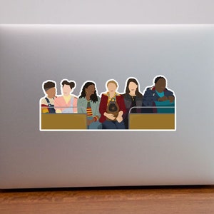 May include: A group of six people, three women and three men, are sitting on a bench. They are all wearing different colored clothing. The people are looking at the camera. The bench is brown and has a gold trim.