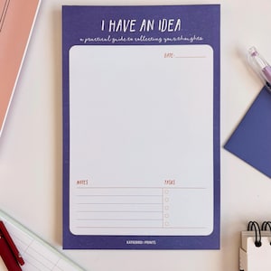 May include: A purple notepad with the text "I HAVE AN IDEA" and "a practical guide to collecting your thoughts." The notepad has sections for notes, tasks, and a date. The brand name "KATIEBIRD: PRINTS" is at the bottom.