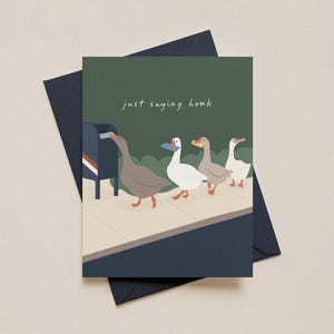 May include: Greeting card with a dark green background and the text "just saying honk". The card features an illustration of four geese walking on a sidewalk, with one putting a letter in a mailbox. The card is on top of a dark blue envelope.