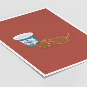 Puede incluir: Un recipiente azul y blanco de yogur natural sobre un fondo rojo con unas gafas de sol aviador doradas.