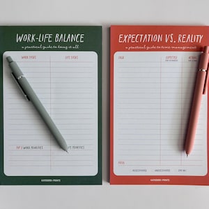 Może przedstawiać: Dwa notatniki z długopisami. Jeden zielony notatnik z napisem "WORK-LIFE BALANCE" i szarym długopisem. Drugi czerwony notatnik z napisem "EXPECTATION VS. REALITY" i r&oacute;żowym długopisem. Oba notatniki mają strony w linie.