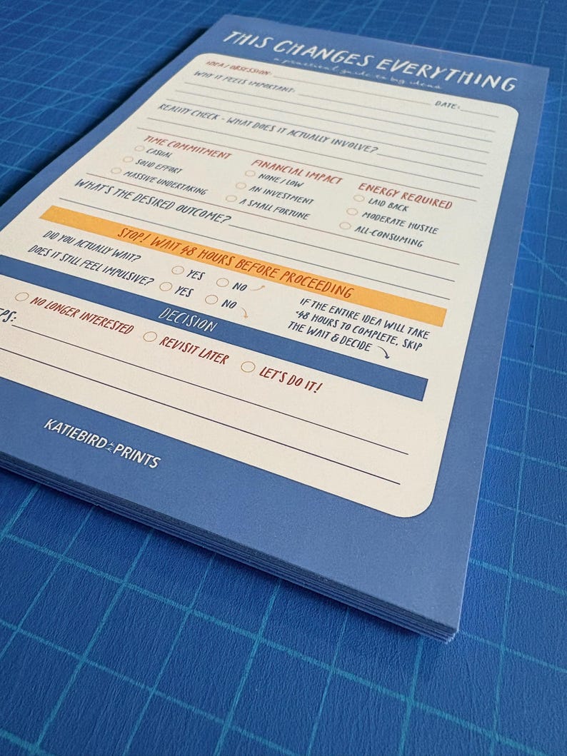 May include: A blue notepad with the text "THIS CHANGES EVERYTHING" at the top. The notepad has sections for idea/question, reality check, time commitment, financial impact, and energy required. The notepad also has the text "STOP! WAIT 48 HOURS BEFORE PROCEEDING".