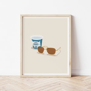 Puede incluir: Una impresi&oacute;n enmarcada con una ilustraci&oacute;n minimalista de un recipiente de yogur azul y gafas de sol marrones sobre un fondo beige.