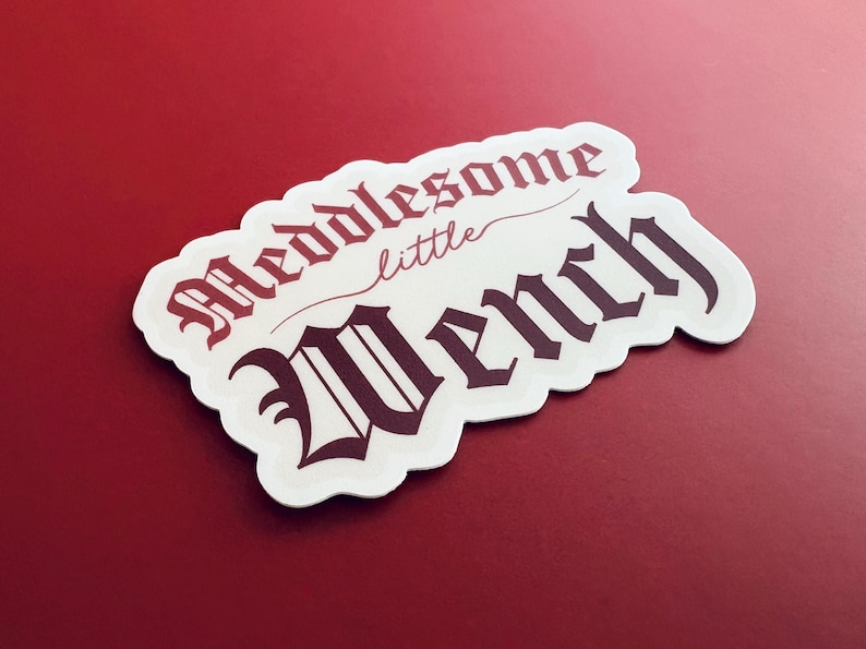 Puede incluir: Pegatina blanca con letras negras y rojas que dicen "Meddlesome little Wench".
