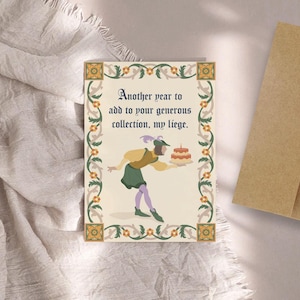 May include: A humorous birthday card with a medieval-style illustration of a person holding a cake. The card reads "Another year to add to your generous collection, my liege."