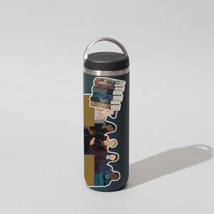 May include: A dark blue stainless steel water bottle with a black lid and a carrying handle. The bottle has a sticker on it featuring a group of people and a stack of books.
