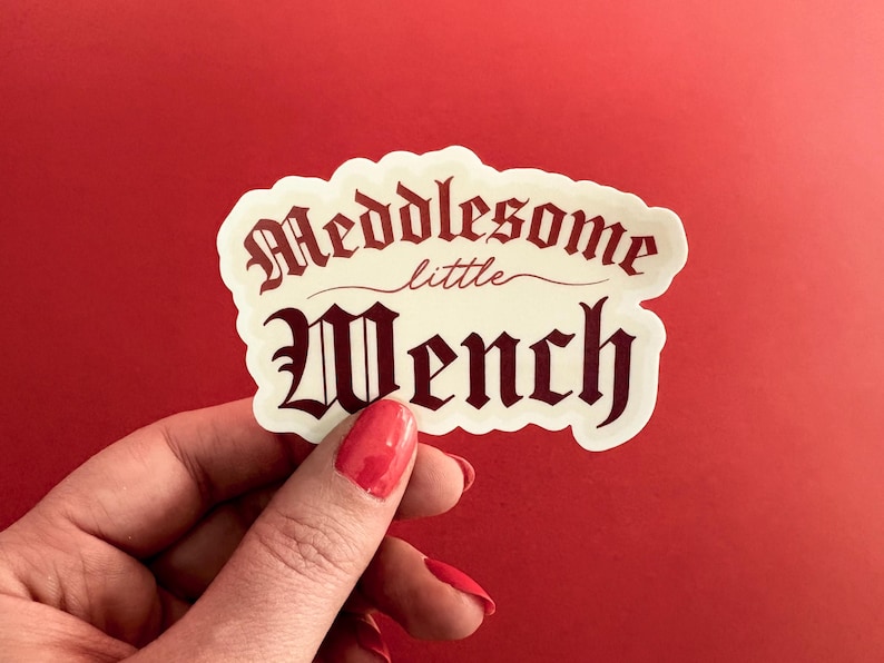 Puede incluir: Una pegatina blanca con el texto "Meddlesome little Wench" en fuente g&oacute;tica roja.