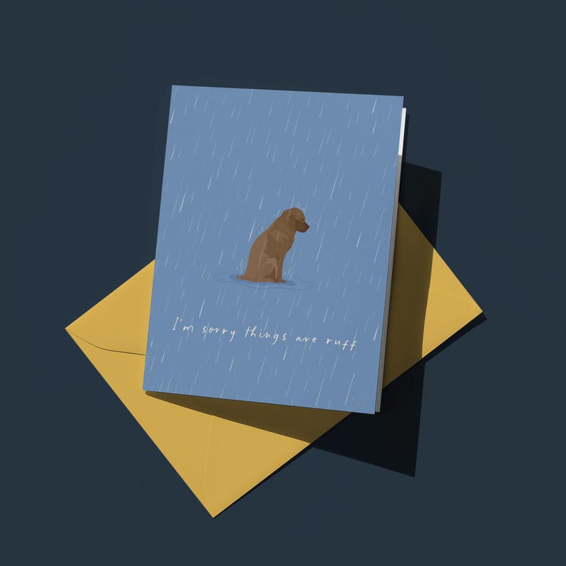 May include: A greeting card with a brown dog in the rain, with the text "I'm sorry things are ruff" on a blue background. The card is paired with a yellow envelope, set against a dark blue backdrop.