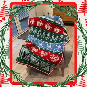Puede incluir: Una manta de ganchillo colorida con un tema navideño de invierno. La manta presenta un esquema de color rojo, verde, blanco y azul con un patrón repetitivo de copos de nieve, árboles y tazas. La manta está drapeada sobre un sillón gris.