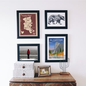 Peut inclure: Un mur de galerie avec quatre impressions encadr&eacute;es. L'impression en haut &agrave; gauche est une carte de l'Overland Track en Tasmanie, en Australie. L'impression en haut &agrave; droite pr&eacute;sente une silhouette d'ours noir avec le texte "Il faut une vraie force pour &ecirc;tre gentil et doux". L'impression en bas &agrave; gauche montre une personne en veste rouge debout sur un quai enneig&eacute; surplombant un lac. L'impression en bas &agrave; droite est une affiche de voyage vintage pour El Capitan dans le parc national de Yosemite.