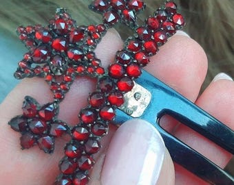 May include: A dark blue hair comb with two prongs. The comb is decorated with a cluster of red garnet stones in the shape of stars.