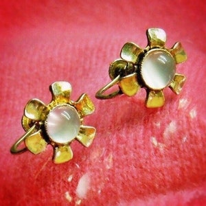 以下が含まれることがあります： 花柄のデザインで、中央に白い石がついた、ゴールドトーンのイヤリングのペアです。