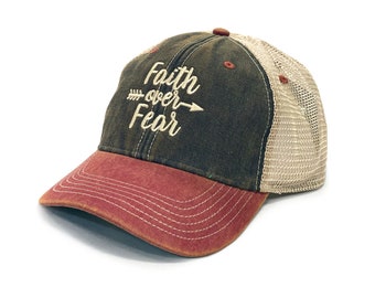 Puede incluir: Una gorra de béisbol verde oscuro y roja con una parte trasera de malla. La parte delantera de la gorra tiene las palabras "Faith over Fear" bordadas en blanco con una flecha apuntando hacia la derecha.