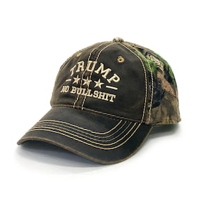May include: A brown camouflage baseball cap with the text "TRUMP - *** - NO BULLSHIT" embroidered in white on the front.