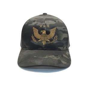 May include: A black and green camouflage trucker hat with a gold embroidered eagle and stars design.
