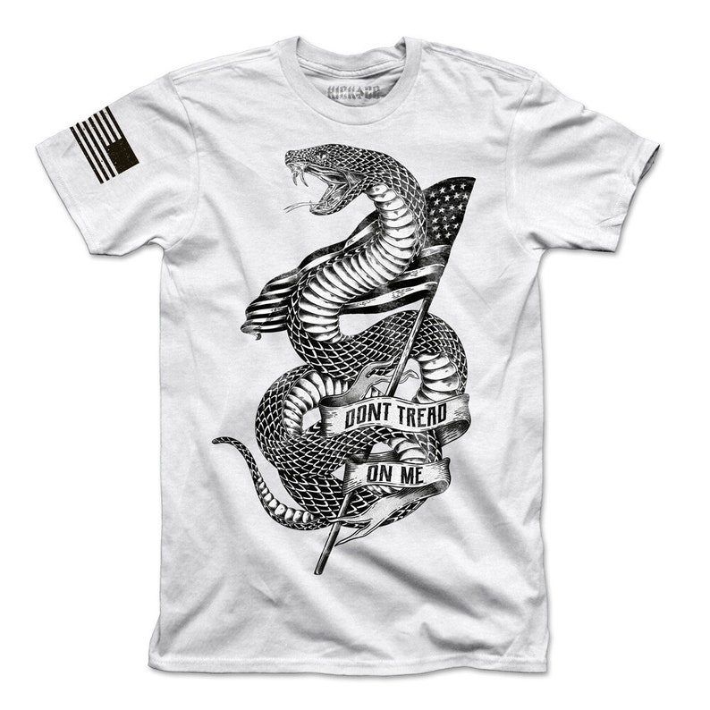 May include: White t-shirt featuring a black and white illustration of a snake wrapped around a flagpole with an American flag. The snake has the words "Don't Tread On Me" written on a banner.