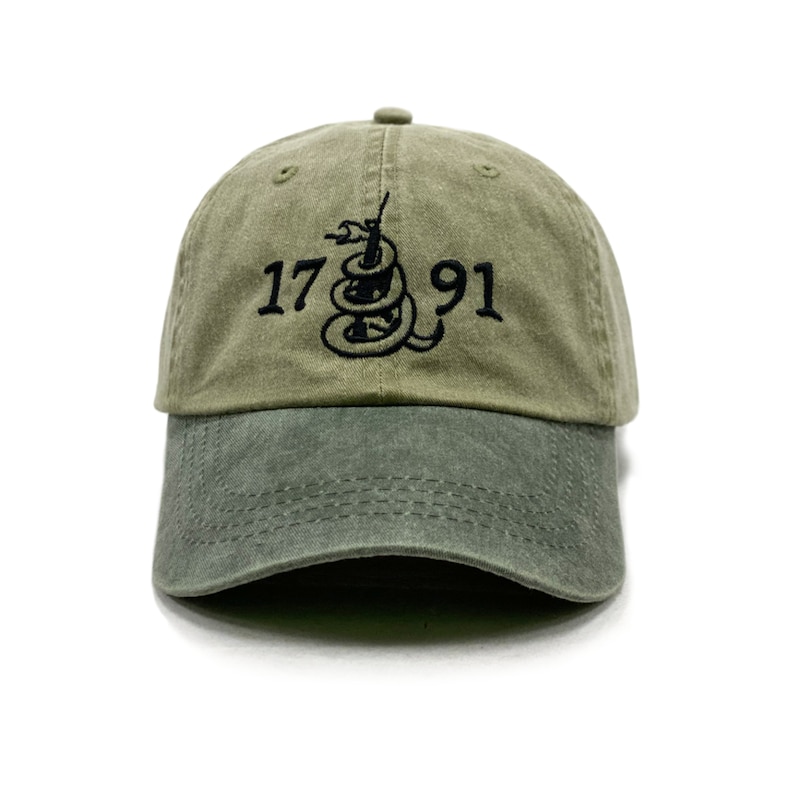 May include: A green baseball cap with a black embroidered snake and the text "1776 91".